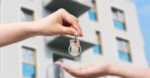 バリの不動産譲渡、所有権、法的事務処理を象徴する、アパートの前でキーホルダーを渡す手。.