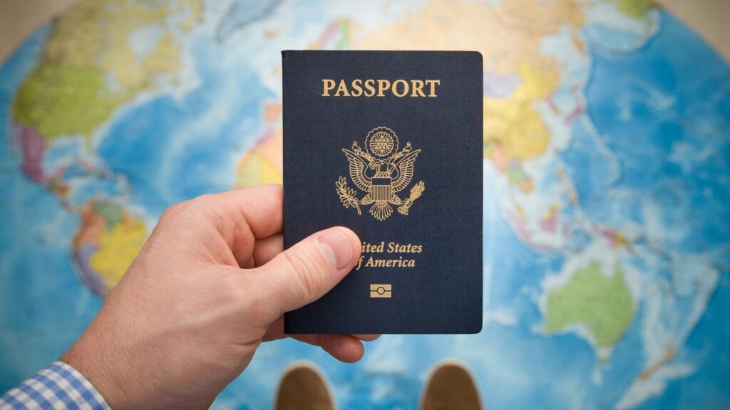 Hand holding a passport in front of a world map, symbolizing the passport mutation process for foreigners updating their stay permit in indonesia.