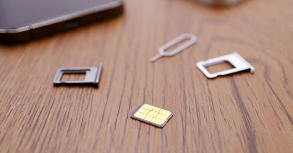 Close-up of a nano sim card with sim tray and ejector tool on a wooden table. Physical sim option for bali travelers.