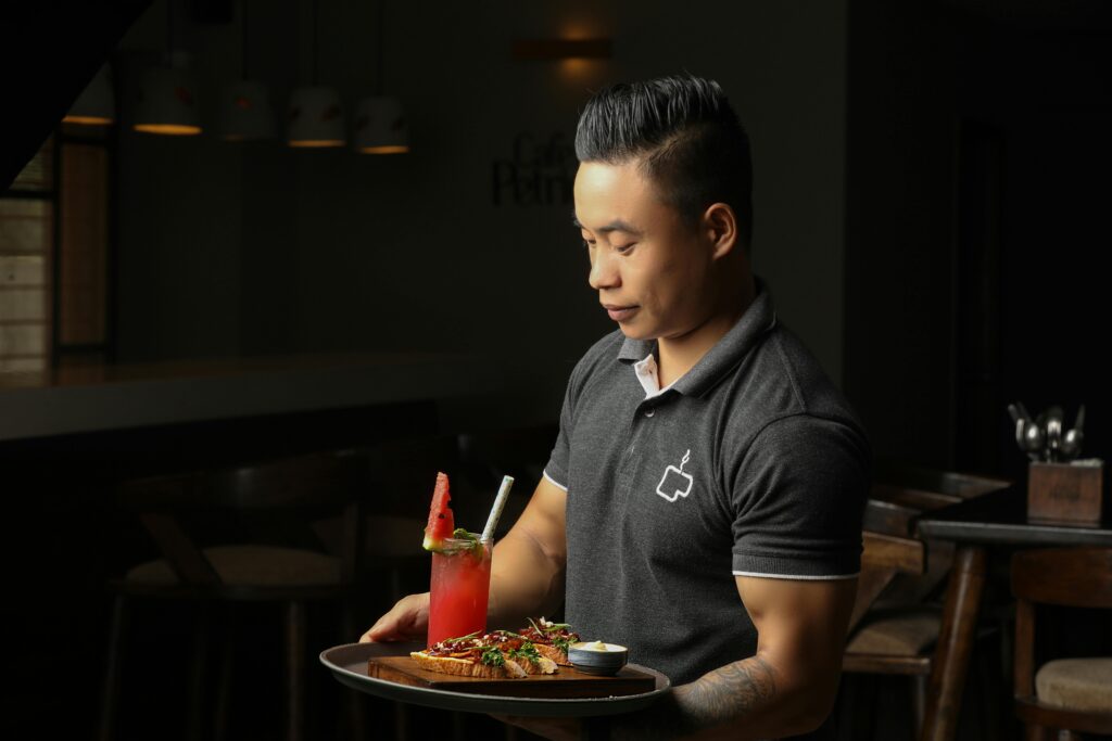 Чоловік-офіціант у ресторані, який несе тацю з їжею та напоями, репрезентує ролі у сфері гостинності, які прив'язані до середньої заробітної плати балійців.