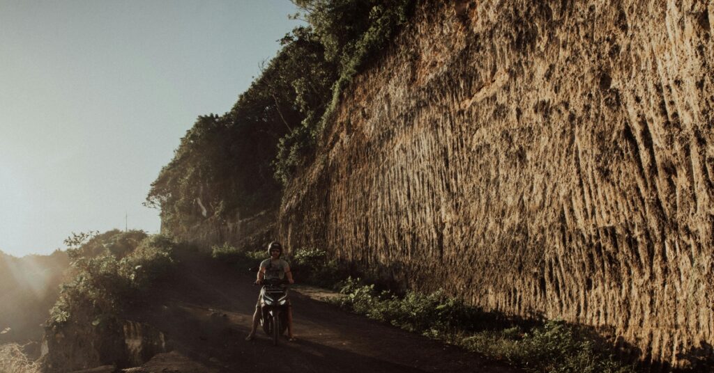 A traveler riding a scooter along a rocky cliff road in bali, symbolizing common travel risks covered by insurance.