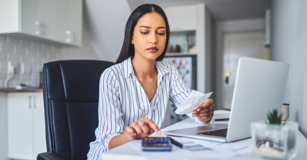 Woman calculating rental expenses with a laptop and receipt, showing hidden costs and monthly rental budgeting in bali.