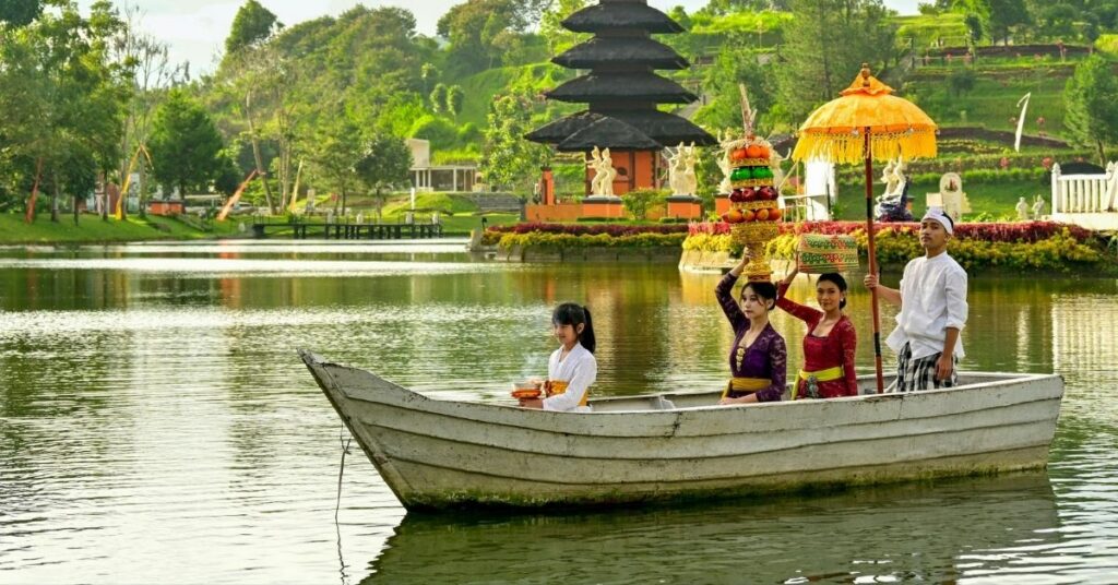 Balinesisk familie i tradisjonelle klær på en liten båt med offergaver og en paraply på en rolig innsjø, for å vise respekt under ritualer i nyepi-sesongen.