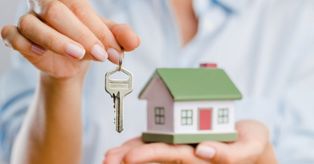 Hand som håller i en husnyckel ovanför en liten modellbostad, som representerar säkrare juridiska alternativ till förvaltararrangemang.
