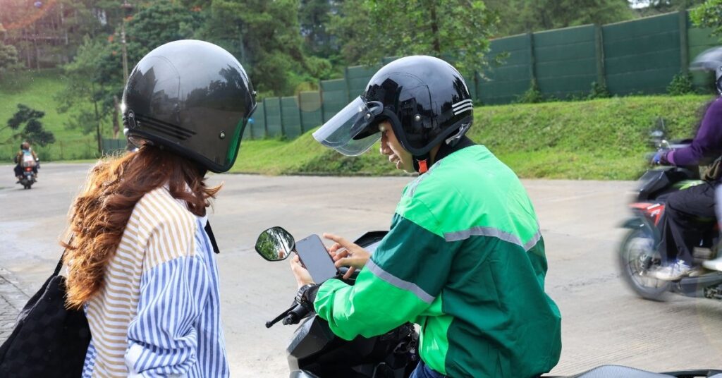 Motorbike ride-hailing driver showing a smartphone to a passenger, suggesting easy in-app payments like grab or gojek.