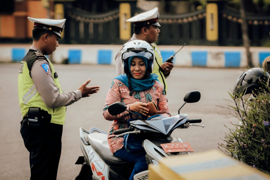 Indonesian traffic police officer speaking to a female motorcyclist wearing a helmet during a roadside check.