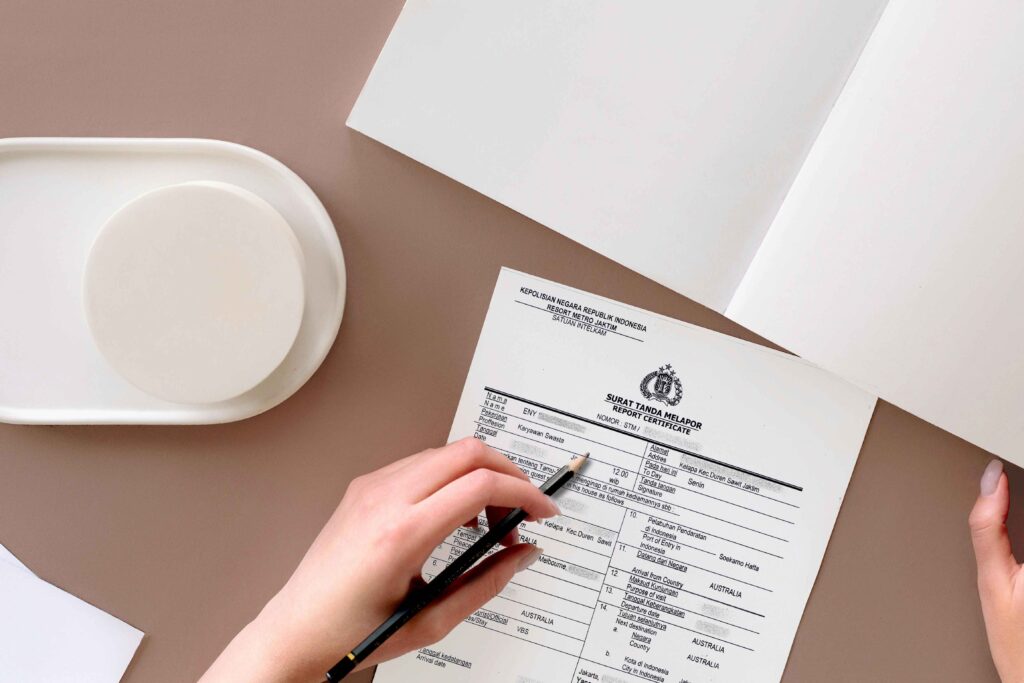 Крупним планом - рука, яка заповнює індонезійську форму звіту про сурат танда мелапор (stm), розміщену на охайному офісному столі.