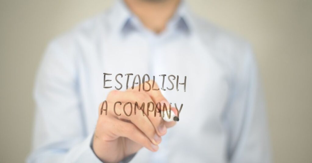 Businessman writing “establish a company” on glass, representing company formation and cross-border business setup.