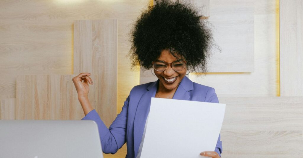 青いブレザーを着た笑顔のプロフェッショナルな女性が、教職契約の成功を象徴する書類を読みながら祝辞を述べている。