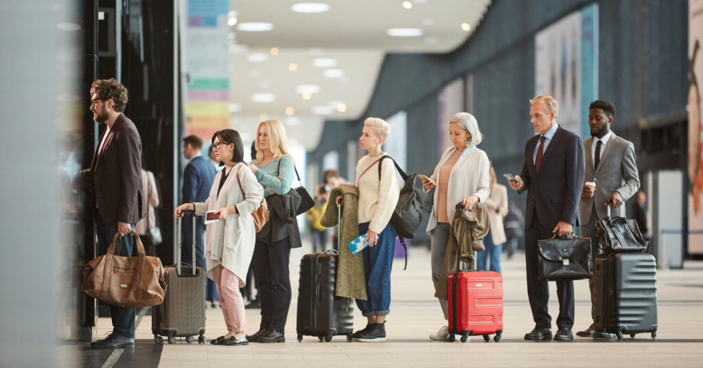 Travelers lined up at an airport terminal with suitcases, waiting for check-in or immigration processing.