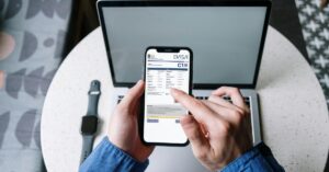 Людина тримає в руках смартфон, на якому відображається затверджена туристична віза Індонезії C1, а на задньому плані - ноутбук і смарт-годинник на столі.