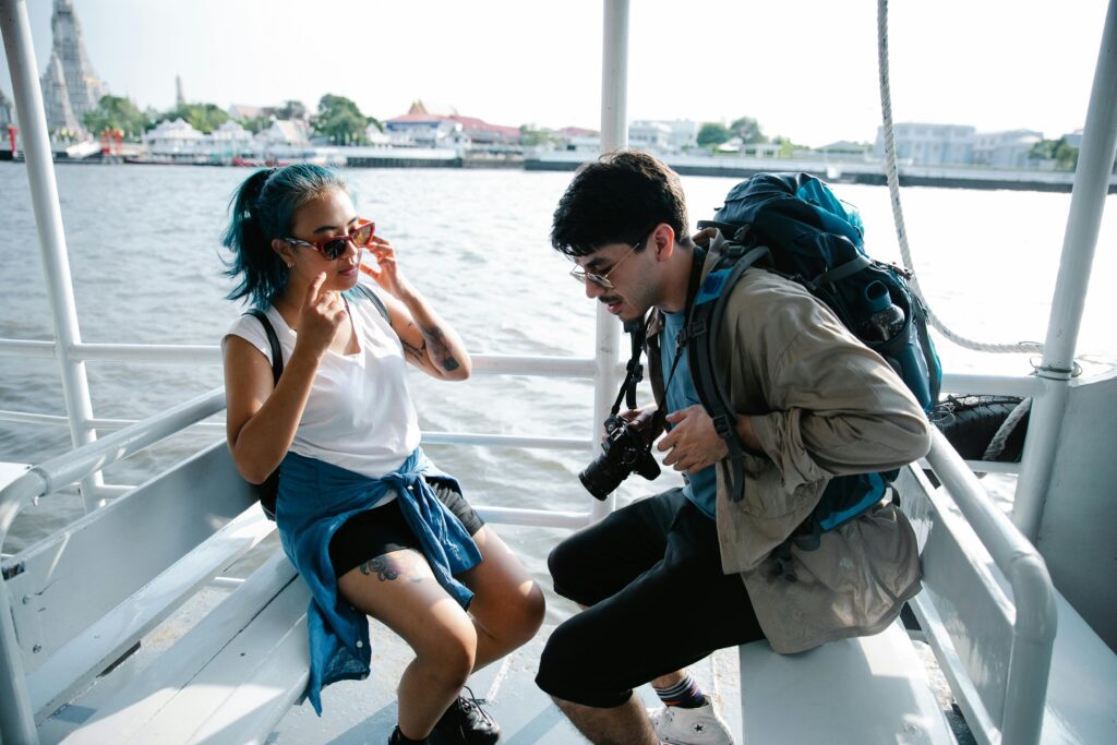 Молоді туристи сидять на човні, готуючись до берегової екскурсії, на тлі води та південно-східної азійської архітектури вдалині.