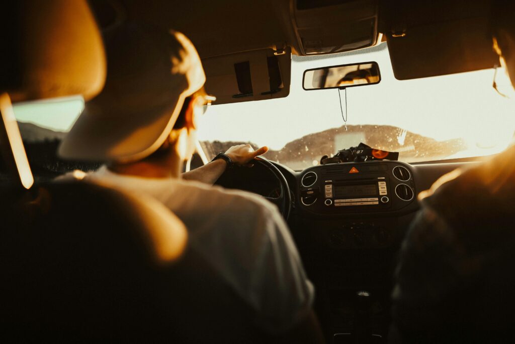 Person driving a car at sunset with golden light shining through the windshield.