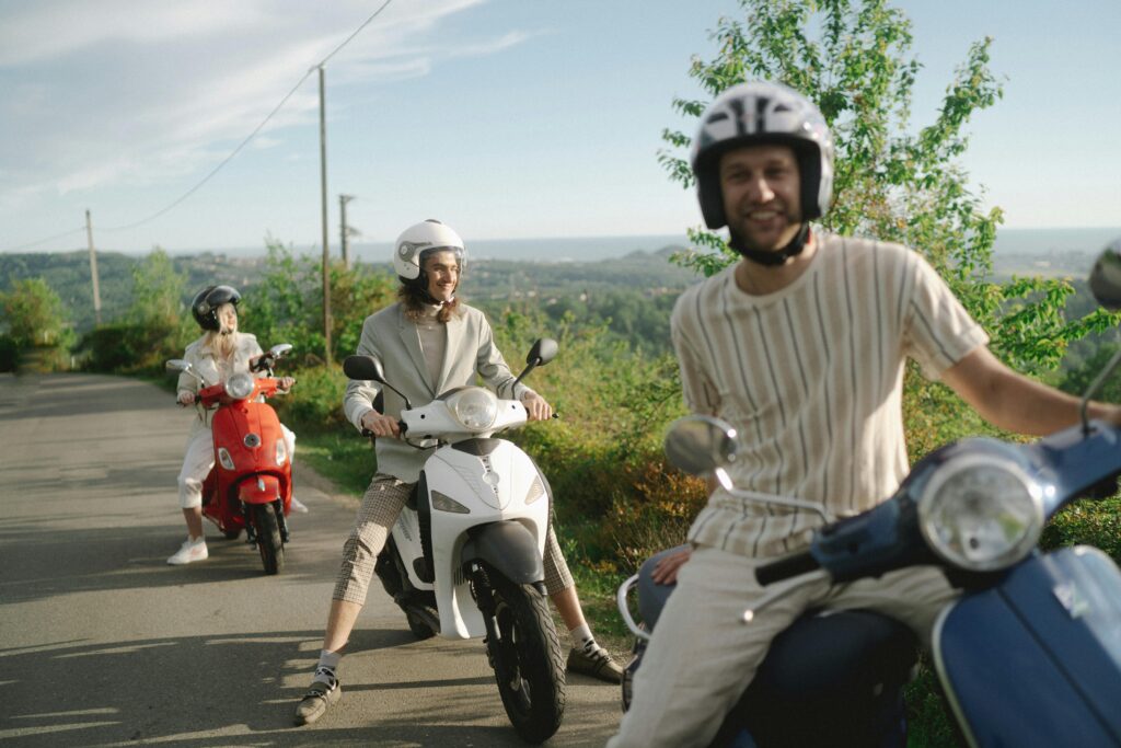 Group of smiling tourists wearing helmets while riding scooters on a scenic road.