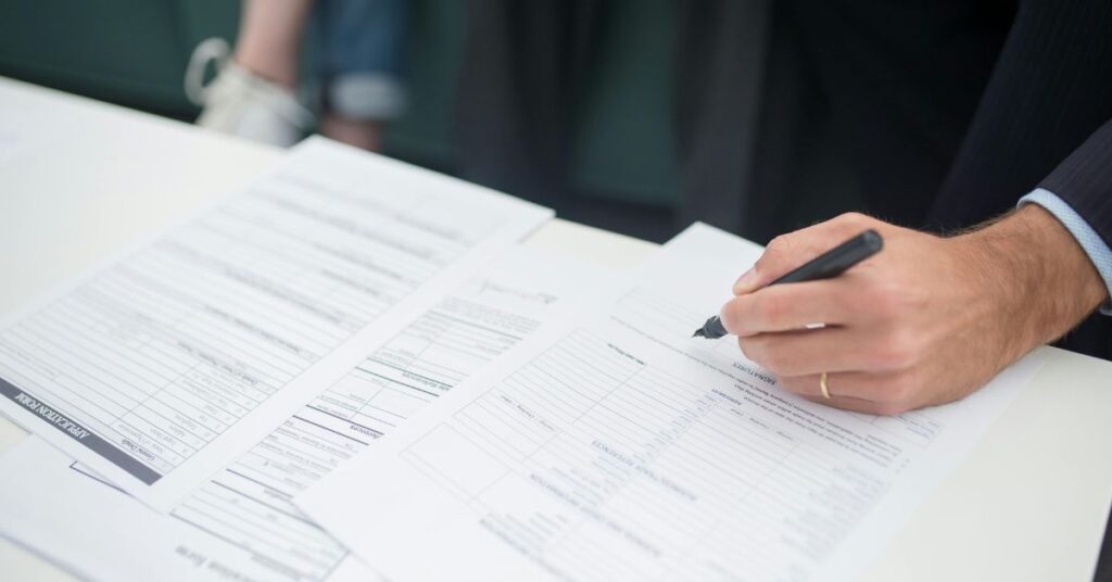Close-up of a person filling out insurance paperwork at a white desk, highlighting the benefits of having travel insurance.