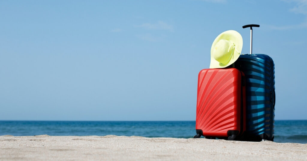 Suitcases and sunhat on a bali beach symbolizing travel plans disrupted by a lost passport in bali.