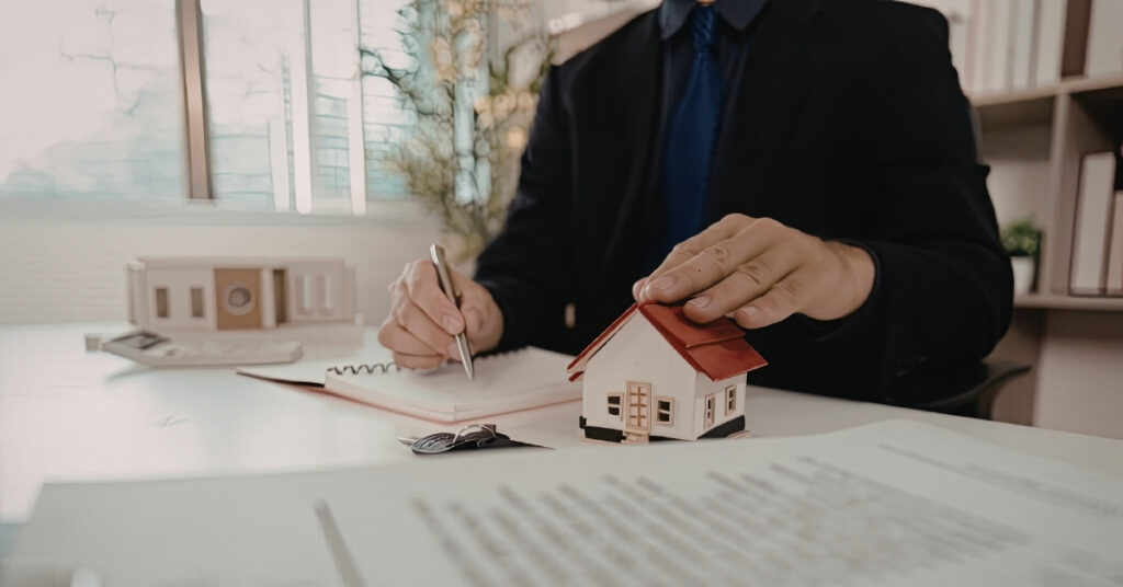 Person som undertecknar juridiskt pappersarbete bredvid ett modellhus, som illustrerar användningen av en förvaltare och de risker som är förknippade med detta i Indonesien.