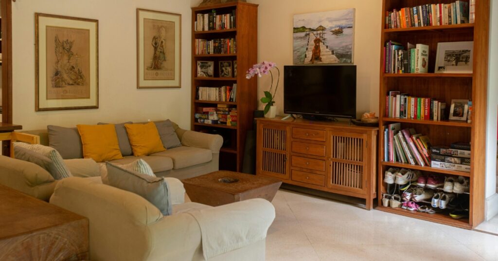 Ett mysigt vardagsrum i en villa på Bali med kuddade soffor, bokhyllor, tv-skåp och väggkonst med tropiska teman.