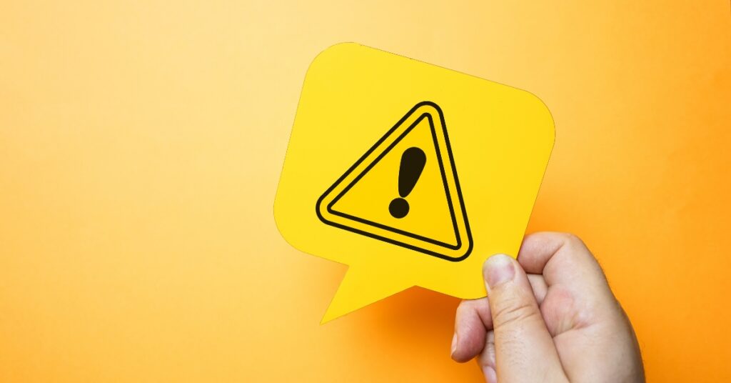 Hand holding a yellow warning icon in a speech bubble on an orange background, representing lkpm compliance risks and sanctions.