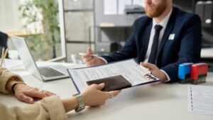 En udlænding, der rækker sit pas til en indvandringsbetjent, mens han gennemgår sine KITA-papirer ved et skrivebord.