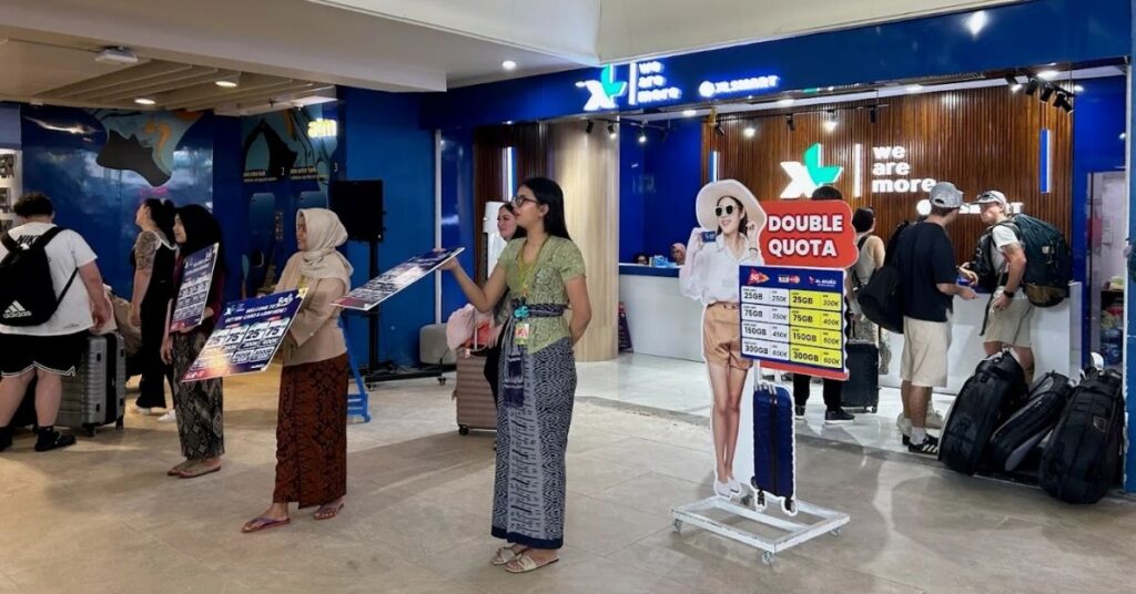 XL Axiata booth at Bali airport with staff selling tourist SIM packages to arrivals.