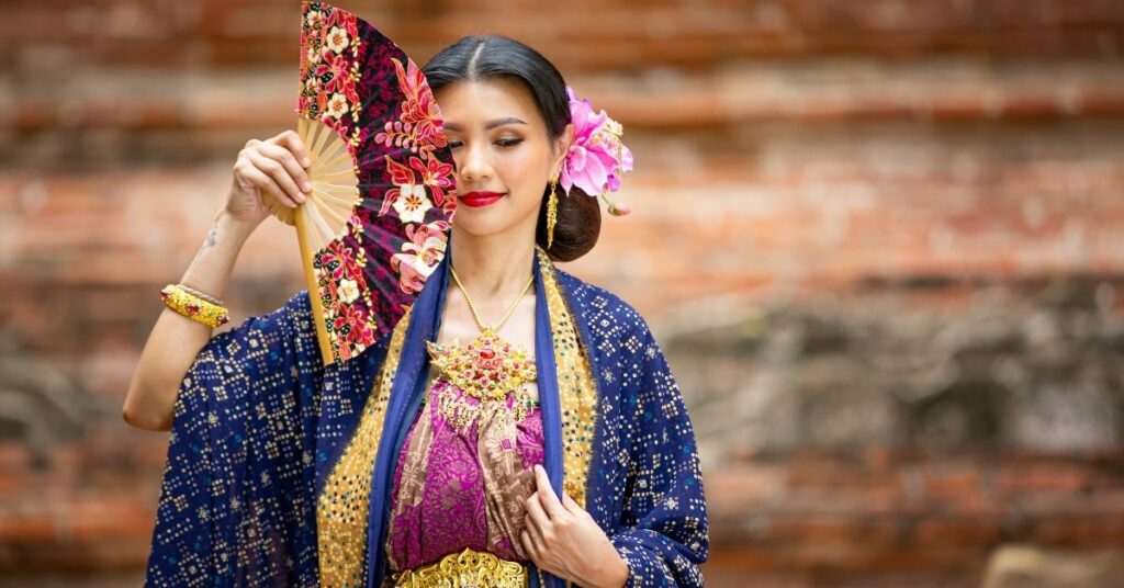 Woman in traditional indonesian attire holding a batik fan, symbolizing indonesian diaspora members reconnecting with cultural roots.