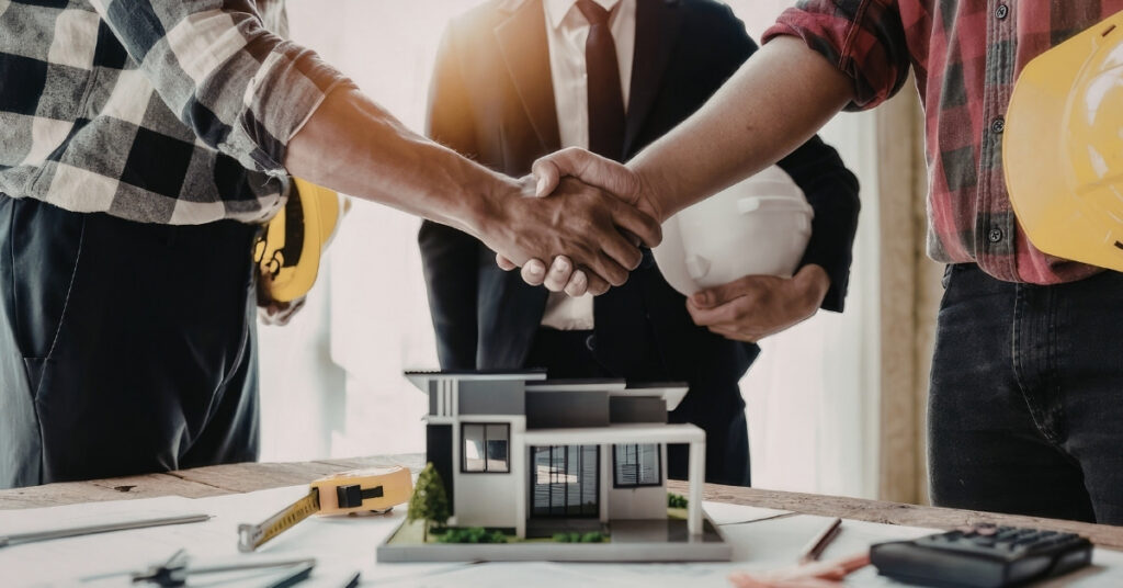 Contractors and advisor shaking hands over a house model during an indonesia building project review