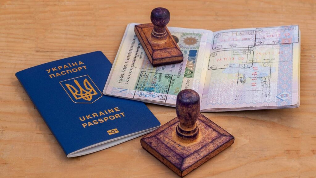 Passaporto accanto a pagine di visto aperte e timbri di immigrazione su un tavolo di legno, a dimostrazione del fatto che la mutazione del passaporto è importante per la validità dei documenti di viaggio e immigrazione.