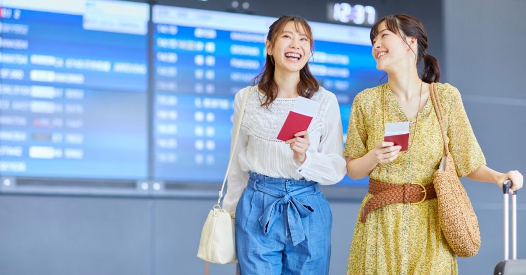 Deux voyageurs heureux tenant leur passeport et riant à l'aéroport, représentant une procédure de visa sans stress avec l'aide d'un agent.